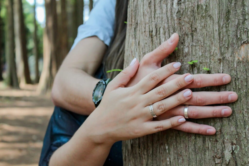 Mãos de um casal entrelaçadas sobre o tronco de uma árvore, simbolizando conexão e amor. Ensaio fotográfico pré-wedding com toque romântico e natural.